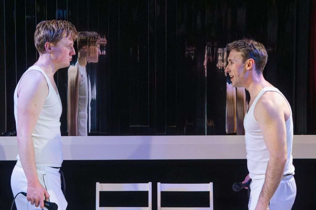 Oliver Maynard and Nick Hyde stand in front of mirrored strips and look angrily at one another