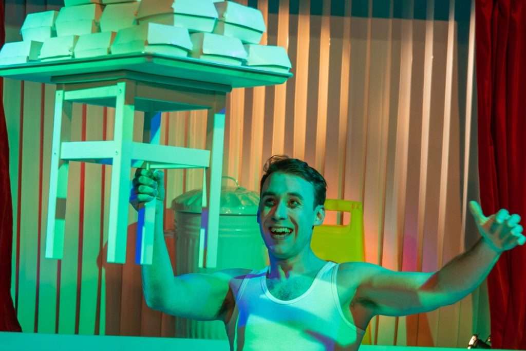 Nick Hyde smiles as he holds a stool stacked with burger boxes aloft