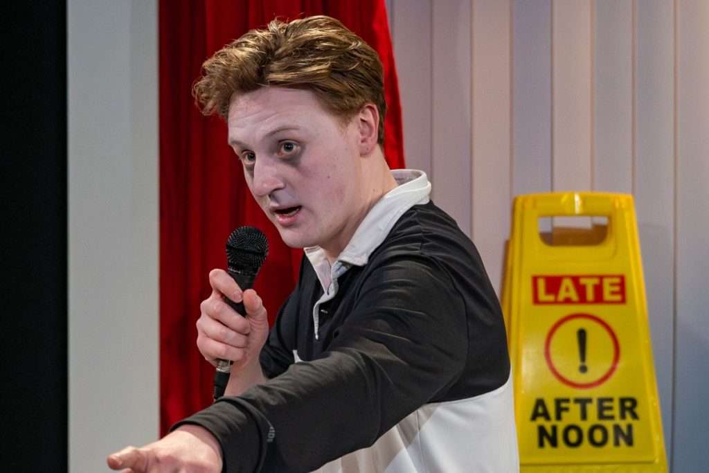 Oliver Maynard points outwards, his other hand holds a microphone