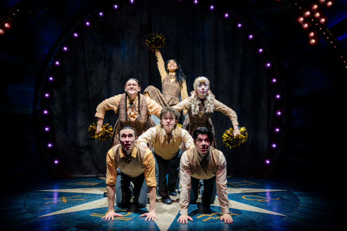 The cast of Ride The Cyclone create the illusion of a human pyramid with Ocean (played by Kayna Montecillo) at the top, grinning and holding a gold pom pom aloft.